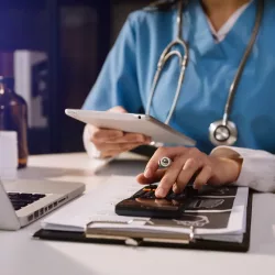 Doctor at desk with computer ipad calculator